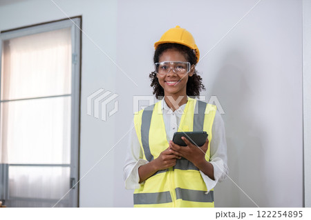Young Engineer at Construction Site with Tablet and Safety Gear, Overseeing Modern Building Project 122254895