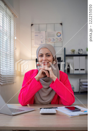 Muslim female entrepreneur wearing hijab sits working with laptop managing personal business in private office. 122255050