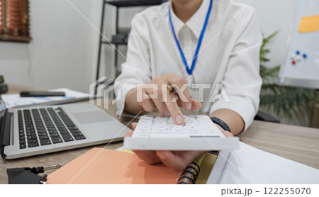 Asian female accountant Use a calculator to calculate business numbers on a white wooden table in the office. 122255070