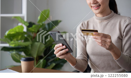 Beautiful young woman uses laptop to shop online, buys things and pays with credit card through phone online banking app. Beautiful young woman uses laptop to shop online, buys things and pays with credit card through phone online banking app. 122255080