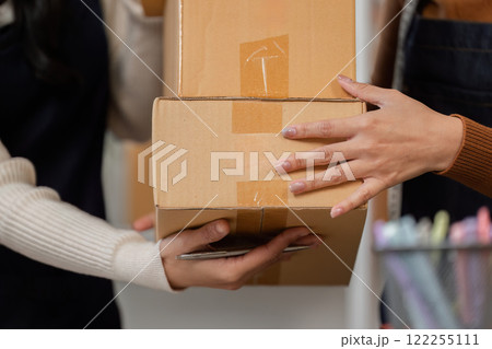 Women exchanging packaged merchandise during an online delivery at a modern workspace Women exchanging packaged merchandise during an online delivery at a modern workspace 122255111