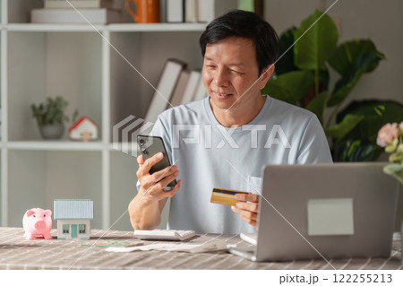 Senior man enjoying online shopping with a credit card and smartphone at home workspace 122255213