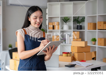 A small SME business owner receives product orders and writes shipping information on cardboard boxes in the home office to prepare for delivery. A small SME business owner receives product orders and writes shipping information on cardboard boxes in the home office to prepare for delivery. 122255351