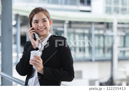 Asian businesswoman drinks coffee and discusses work on the phone in the hallway outside the office. Asian businesswoman drinks coffee and discusses work on the phone in the hallway outside the office. 122255413