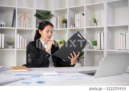 Focused Asian female accountant doing paperwork in office with plan documents on desk Focused Asian female accountant doing paperwork in office with plan documents on desk 122255414