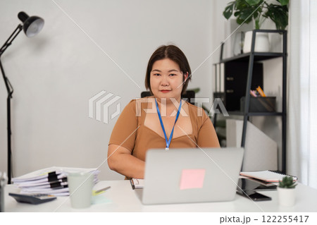Young Female Office Worker Focused at Her Desk in a Modern Office Environment with Laptop and Documents Young Female Office Worker Focused at Her Desk in a Modern Office Environment with Laptop and Documents 122255417