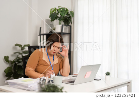 Stressed Businesswoman at Work Desk with Laptop and Documents in Modern Office Setting Stressed Businesswoman at Work Desk with Laptop and Documents in Modern Office Setting 122255421