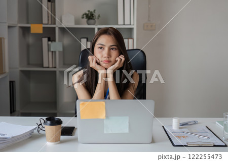 Pensive Asian businesswoman feeling overwhelmed while working at a desk in a contemporary office Pensive Asian businesswoman feeling overwhelmed while working at a desk in a contemporary office 122255473