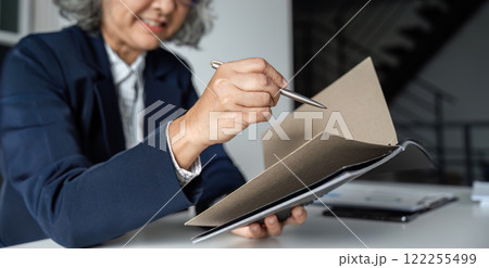 Elderly Businesswoman Engaged in Reading a Book at Her Desk in a Modern Office Setting Elderly Businesswoman Engaged in Reading a Book at Her Desk in a Modern Office Setting 122255499
