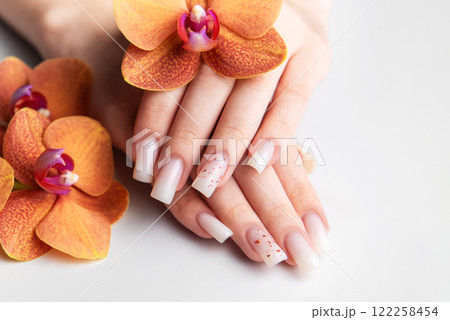 Woman showing stylish white nails with orange orchid decoration 122258454