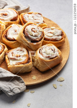 Delicious cinnamon rolls with white icing and almond flakes resting on wooden plate 122258459