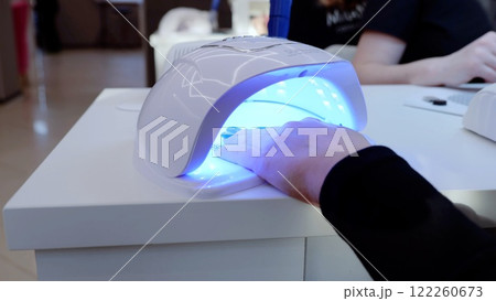 Beautician using an ultraviolet lamp to cure gel nail polish during a manicure treatment at a professional beauty salon Beautician using an ultraviolet lamp to cure gel nail polish during a manicure treatment at a professional beauty salon 122260673
