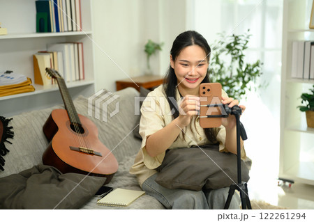 Young musician setting up her smartphone on a tripod, preparing to record her guitar performance Young musician setting up her smartphone on a tripod, preparing to record her guitar performance 122261294