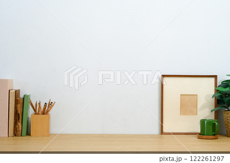 Rustic workspace with pencil holder, vintage books, a coffee mug, and picture frame against white wall 122261297