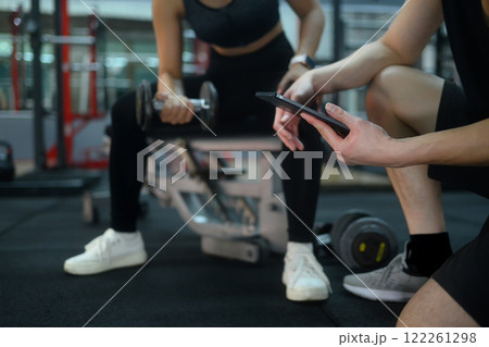 Personal trainer holding digital tablet to assess client performance during a weightlifting exercise 122261298