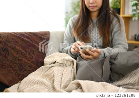 Young woman using her smartphone while lounging on a sofa with blankets and cushions Young woman using her smartphone while lounging on a sofa with blankets and cushions 122261299