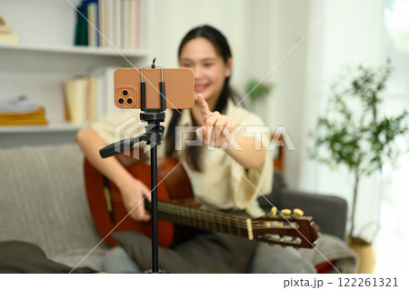 Young musician setting up her smartphone on a tripod, preparing to record her guitar performance Young musician setting up her smartphone on a tripod, preparing to record her guitar performance 122261321