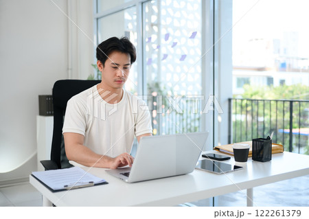 Young entrepreneur working intently on laptop at desk in a contemporary office 122261379