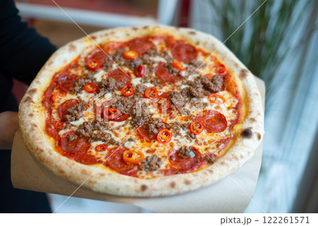 Excellent Italian pizza holding in hands with salami, chilli peppers, much cheese Excellent Italian pizza holding in hands with salami, chilli peppers, much cheese 122261571