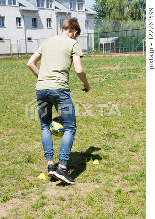 Teenager practicing soccer skills outdoors, juggling ball near markers. Sunny day, grassy field. Teenager practicing soccer skills outdoors, juggling ball near markers. Sunny day, grassy field. 122261599