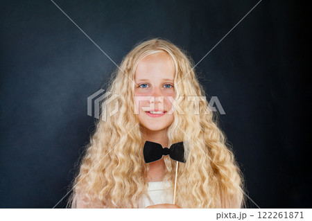 Beautiful young girl posing with photo booth props bow on black background Beautiful young girl posing with photo booth props bow on black background 122261871