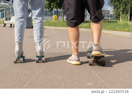 Young couple rollerblading and skateboarding in park. Happy and joyful girl and man doing sports together on warm summer day. High quality photo 122263516