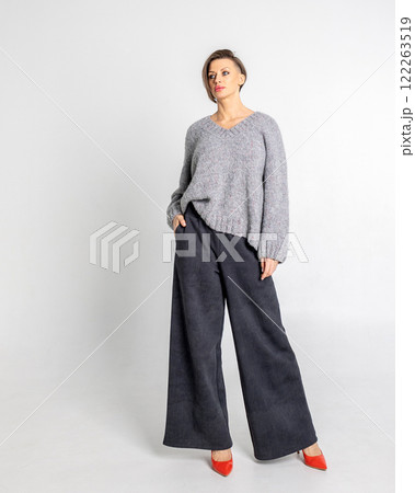Portrait beautiful woman of model appearance. Girl in grey jumper, black trousers, red shoes on grey background. Pretty female with trendy makeup posing in studio. Vertical photo. Portrait beautiful woman of model appearance. Girl in grey jumper, black trousers, red shoes on grey background. Pretty female with trendy makeup posing in studio. Vertical photo. 122263519