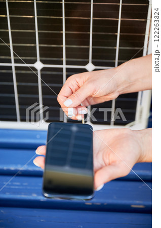 Close up view of woman charging her phone from solar battery. Young female using solar panel charger for mobile devices. Integration of sustainable renewable energy into everyday life. Close up view of woman charging her phone from solar battery. Young female using solar panel charger for mobile devices. Integration of sustainable renewable energy into everyday life. 122263824