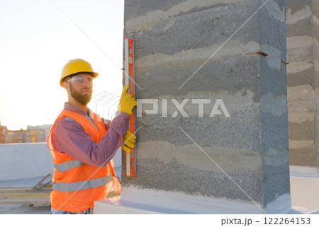 Construction worker using spirit level on building site at sunset 122264153