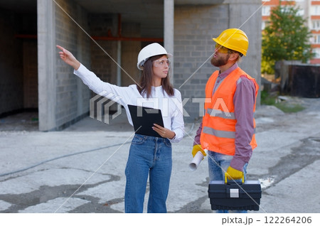 Female architect pointing at something while discussing with construction worker at building site 122264206