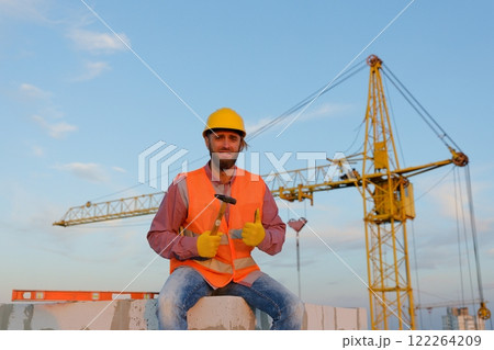 Construction worker sitting and holding hammer at construction site 122264209