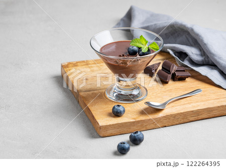 Chocolate pudding in a glass with fresh blueberries and mint on a wooden board on a light background 122264395