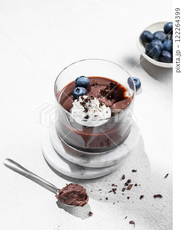 Chocolate pudding in a glass with whipped cream and fresh blueberry on a light background 122264399