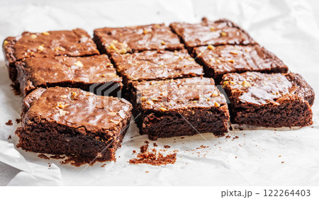 Chocolate brownie with nuts cut into pieces on baking paper close-up with morning light. Chocolate brownie with nuts cut into pieces on baking paper close-up with morning light. 122264403