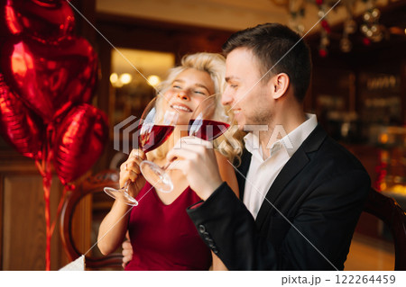 Man and woman on date in restaurant sitting table holding glasses drinking red wine cheers flirting. Man and woman on date in restaurant sitting table holding glasses drinking red wine cheers flirting. 122264459