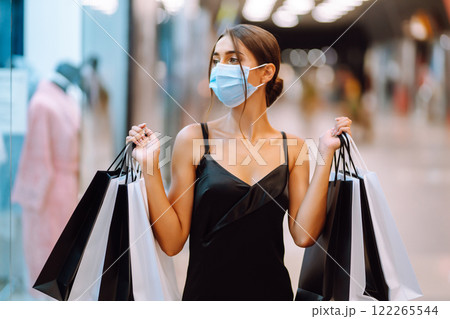 Fashionable woman in protective medical mask with shopping bags walking in the mall. Covid-19. Fashionable woman in protective medical mask with shopping bags walking in the mall. Covid-19. 122265544