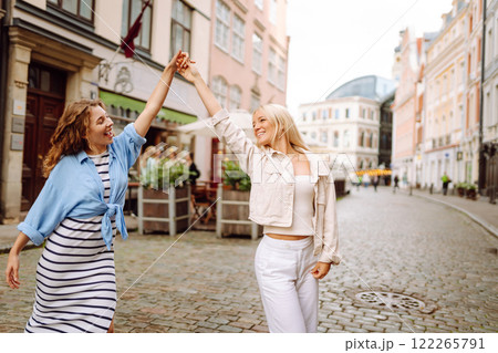 Smiling girlfriends are having fun on a sunny day on the streets of the city. Active lifestyle. Smiling girlfriends are having fun on a sunny day on the streets of the city. Active lifestyle. 122265791