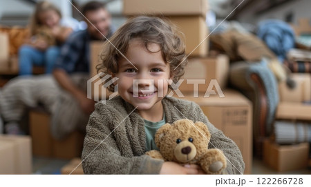 Moving. A caucasian family moving into their new home, with a smiling child holding a teddy bear in the foreground amongst cardboard boxes and furniture around them 122266728