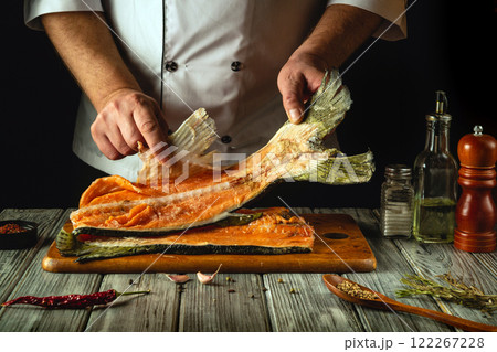 This dynamic kitchen moment captures a skilled chef filleting a fresh piece of fish on a wooden cutting board, surrounded by spices and herbs. The warm ambiance enhances the culinary artistry This dynamic kitchen moment captures a skilled chef filleting a fresh piece of fish on a wooden cutting board, surrounded by spices and herbs. The warm ambiance enhances the culinary artistry 122267228
