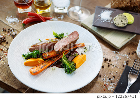 Duck fillet with sweet potato cream, roasted carrots, kale, beet-port sauce on white plate. Grilled and roasted poultry closeup served on a table for lunch in modern cuisine gourmet restaurant. 122267411