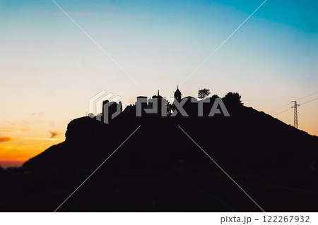 The castle on the mountain against the sunset sky. Abstract village, town in sunrise. Houses and towers on a hill at dusk, in twilight. Sunlight sky. 122267932