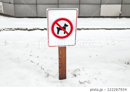 A white wooden warning sign with red pictogram of a dog prohibiting dog walking on a city street in winter. Prohibition of dogs on a lawn Public space 122267934