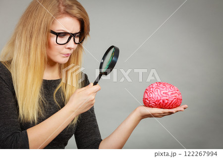 Woman holding magnifying glass investigating brain Woman holding magnifying glass investigating brain 122267994