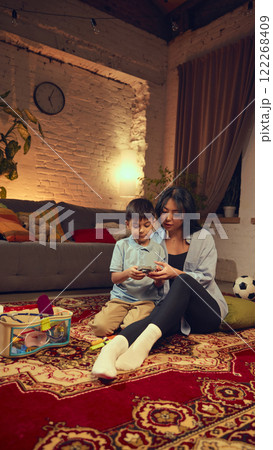 Children, boy and girl sitting on floor in cozy living room with mother, children pretending to be doctors. Dental care, toy medical kit Children, boy and girl sitting on floor in cozy living room with mother, children pretending to be doctors. Dental care, toy medical kit 122268409
