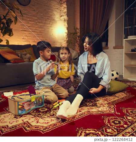 Children, boy and girl sitting on floor in cozy living room with woman lying on floor, children pretending to be doctors. Physician Children, boy and girl sitting on floor in cozy living room with woman lying on floor, children pretending to be doctors. Physician 122268412