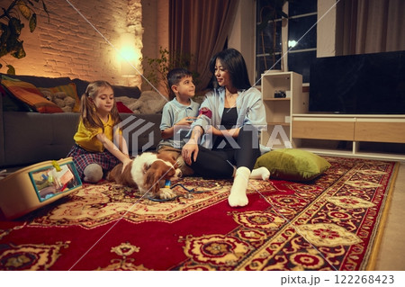 Children, boy and girl with woman sitting on floor in cozy living room in the evening and playing doctors and vet with dog and medical toy kit 122268423