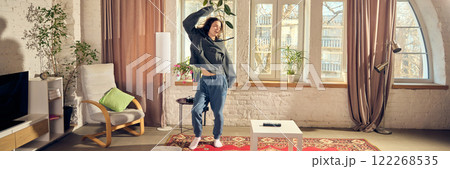 Young man in casual stylish clothes, oversized hoodie and pants, listening to music in headphone and joyfully dancing at home in living room Young man in casual stylish clothes, oversized hoodie and pants, listening to music in headphone and joyfully dancing at home in living room 122268535