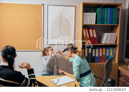 Female doctor with headlight performing nose and throat examination on young girl, highlighting ENT-focused healthcare. 122268620