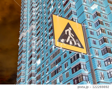 Pedestrian yellow sign against a tall blue apartment building in an urban environment. Road safety and infrastructure. Inverted photo. Cross the road. 122269892