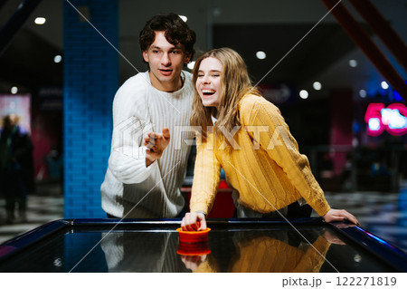 Friends enjoying a fun moment while playing air hockey in an arcade 122271819